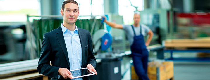 A smiling man in a manufacturing warehouse holding an ipad that contains real-time SPC process data