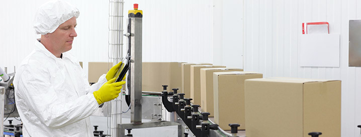 Man examining data on a small screen overlooking a product line using his new quality assurance software